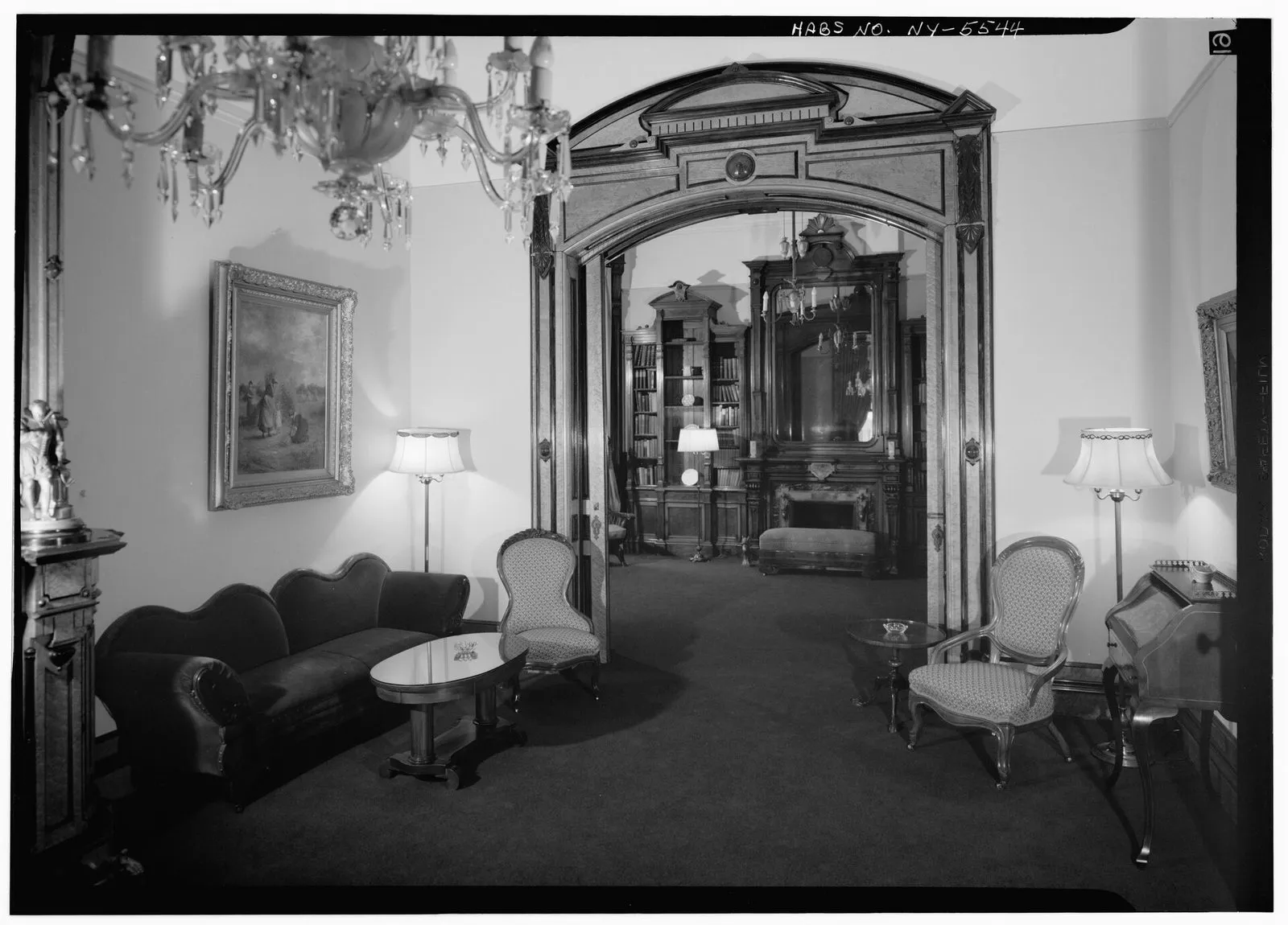 A panelled sitting room opening into a library through a wide doorway.